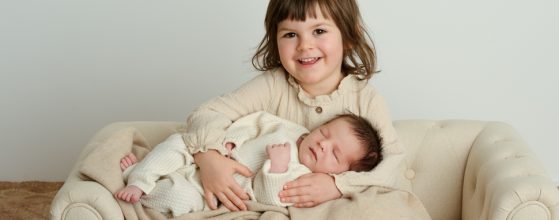 Großes Geschwisterkind kuschelt beim Neugeborenen-Shooting mit seinem kleinen Geschwisterbaby